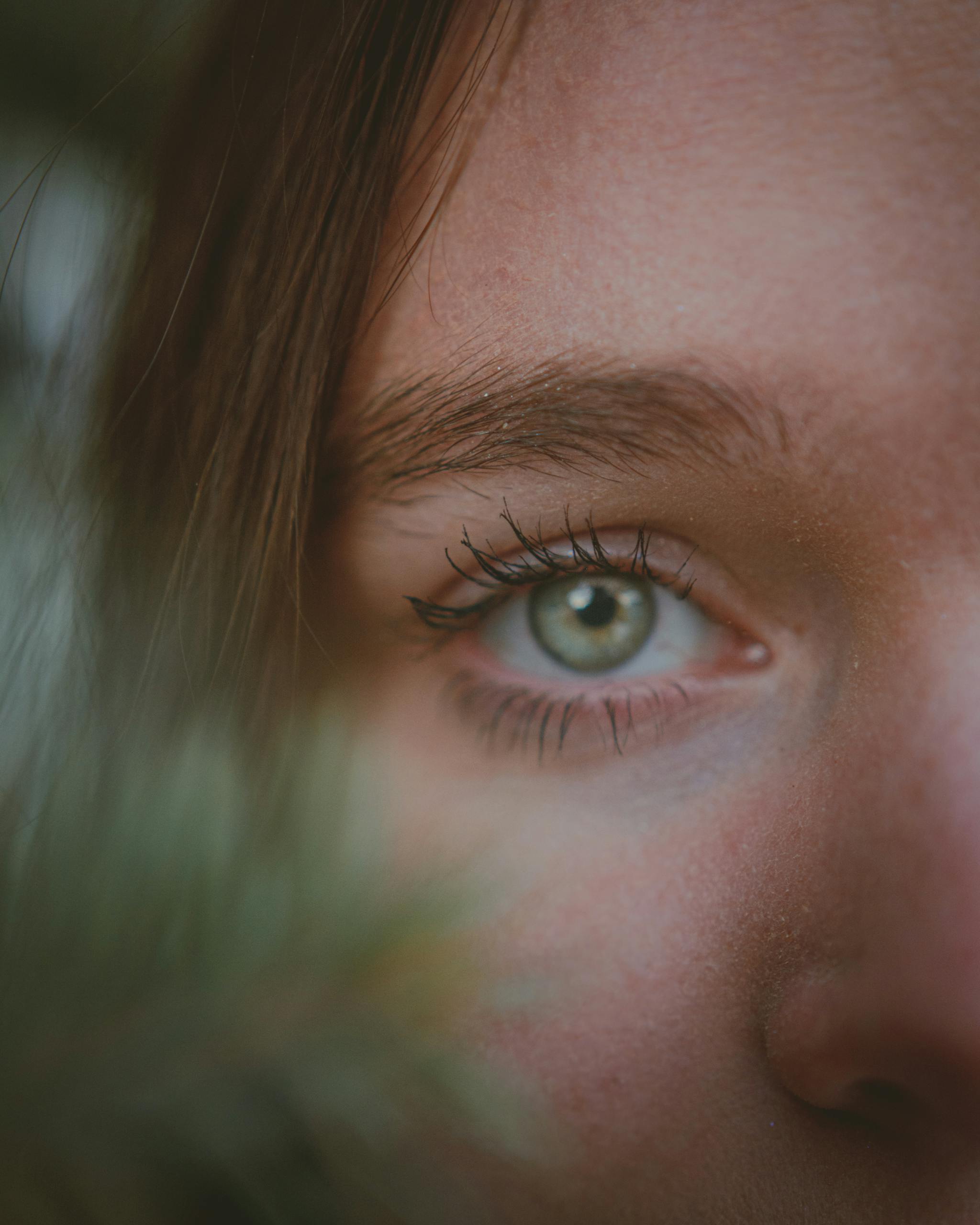 Extreme close-up of a young woman with green eyes, focusing on one eye with selective blur.